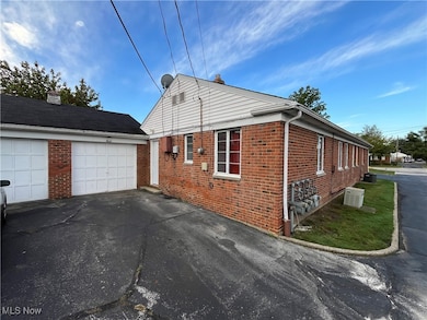 View of side of home with a garage, brick siding, a chimney, and driveway