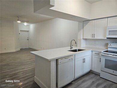 Kitchen featuring white cabinetry, sink, dark hardwood / wood-style flooring, kitchen peninsula, and white appliances