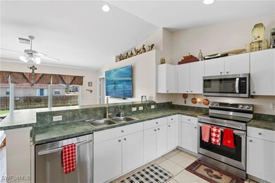 Kitchen featuring appliances with stainless steel finishes, light tile patterned floors, dark countertops, a peninsula, and white cabinets
