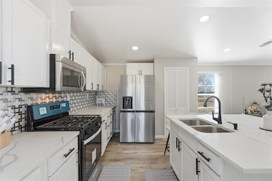 Kitchen with stainless steel appliances, white cabinetry, light stone countertops, light wood-type flooring, and recessed lighting