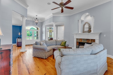 Living room with hardwood flooring, decorative columns, ceiling fan, crown molding, and gas fireplace. Downstairs living area HVAC new in 2025.