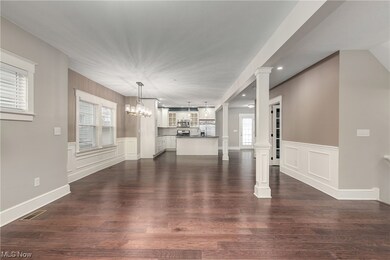 Open concept living room / dining room featuring decorative columns, an inviting chandelier, and dark hardwood floors, with a view of the kitchen.