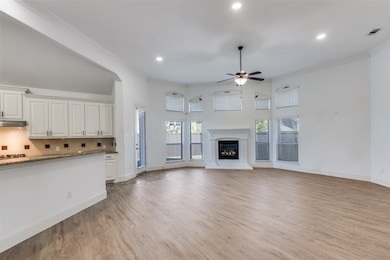 Unfurnished living room featuring crown molding, light wood-style floors, a glass covered fireplace, ceiling fan, and recessed lighting