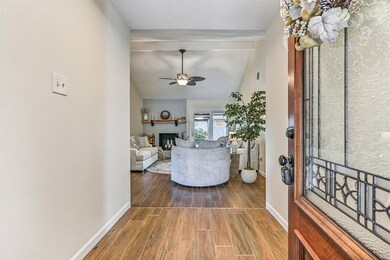 The entryway opens into a bright family room with a ceiling fan and a charming fireplace. Natural light fills the room through large windows, complementing the inviting atmosphere.