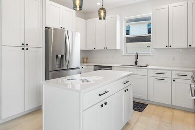 Kitchen with stainless steel appliances, decorative light fixtures, white cabinetry, light wood-style flooring, and a kitchen island