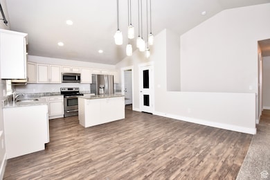 Kitchen with a kitchen island, decorative light fixtures, stainless steel appliances, dark wood finished floors, and light stone counters
