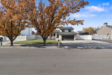 View of property hidden behind natural elements with driveway, solar panels, a gate, roof with shingles, and an attached garage