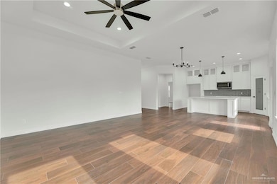 Unfurnished living room with ceiling fan with notable chandelier, visible vents, recessed lighting, and a tray ceiling