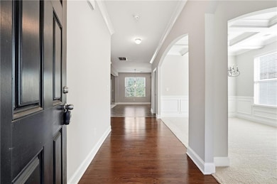 Hall featuring arched walkways, beamed ceiling, dark wood-style floors, coffered ceiling, and a decorative wall