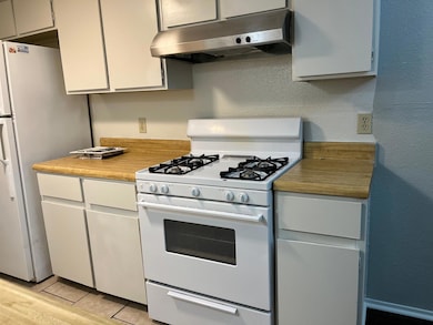 Kitchen featuring a textured wall, white appliances, under cabinet range hood, light countertops, and light tile patterned floors