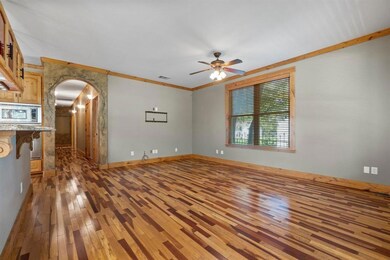 Unfurnished living room with arched walkways, crown molding, dark wood-type flooring, and ceiling fan