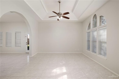 Unfurnished room with a tray ceiling, arched walkways, and light tile patterned floors