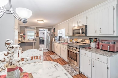Kitchen featuring appliances with stainless steel finishes, crown molding, wood finished floors, light countertops, and white cabinets