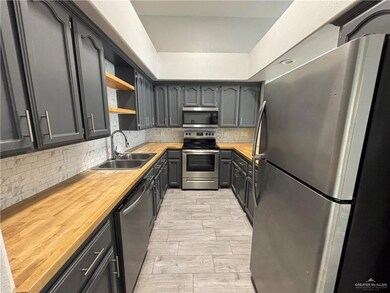 Kitchen with tasteful backsplash, open shelves, a sink, butcher block counters, and appliances with stainless steel finishes