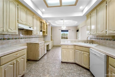 Kitchen with dishwasher, under cabinet range hood, a raised ceiling, a peninsula, and decorative backsplash