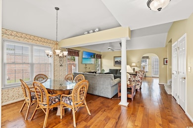 Dining space with hardwood / wood-style flooring, arched walkways, decorative columns, lofted ceiling, and a chandelier