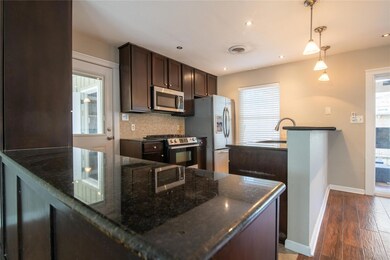 Kitchen featuring dark brown cabinetry, a peninsula, dark stone countertops, backsplash, and appliances with stainless steel finishes
