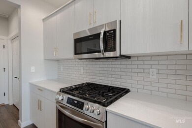 Kitchen featuring stainless steel appliances, tasteful backsplash, modern cabinets, dark wood-type flooring, and light stone counters