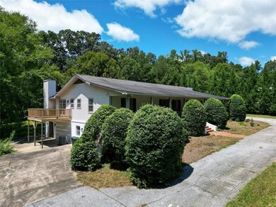 View of front facade with a chimney, a wooden deck, driveway, and a forest view