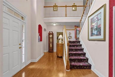 Entryway featuring wood finished floors, a towering ceiling, stairs, arched walkways, and baseboards