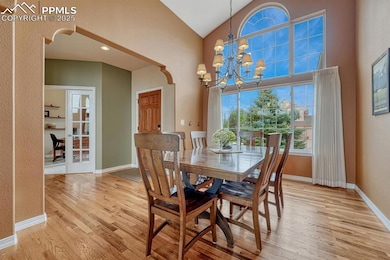 Dining area featuring light wood-style flooring, a chandelier, baseboards, and high vaulted ceiling