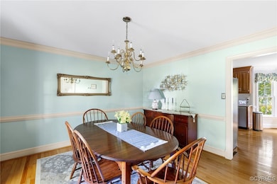 Dining room with light wood-type flooring, an inviting chandelier, and ornamental molding