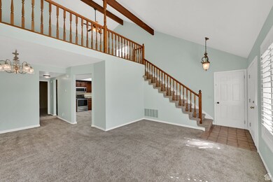 Entrance foyer with high vaulted ceiling, light carpet, a chandelier, beam ceiling, and stairway