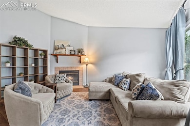Living area featuring a tiled fireplace, a textured ceiling, wood finished floors, and lofted ceiling