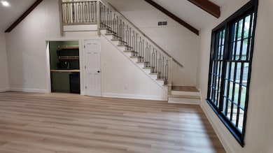 Unfurnished living room with high vaulted ceiling, light wood-style flooring, beamed ceiling, stairs, and wooden walls
