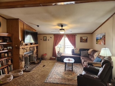 Carpeted living room featuring crown molding, a stone fireplace, and a ceiling fan