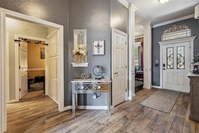 Entryway with wood finished floors, ornate columns, baseboards, and crown molding