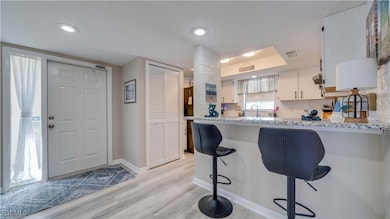 Kitchen with a breakfast bar area, white cabinetry, granite countertops, light wood-style floors, and a peninsula