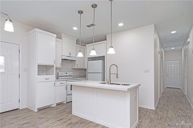 Kitchen featuring hanging light fixtures, white appliances, sink, and an island with sink