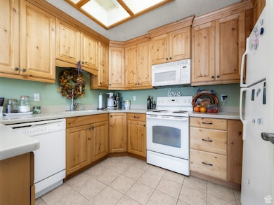 Kitchen with white appliances, light countertops, light tile patterned floors, and light brown cabinets