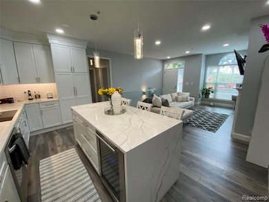 Kitchen with tasteful backsplash, light stone countertops, decorative light fixtures, white cabinets, and a center island