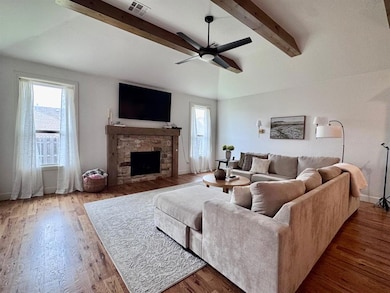Living area featuring healthy amount of natural light, ceiling fan, a stone fireplace, and wood finished floors