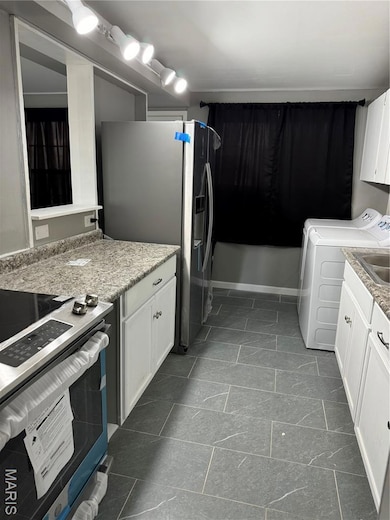 Kitchen with stainless steel appliances, white cabinetry, and light stone counters