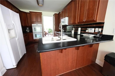 Kitchen with white appliances, a peninsula, dark wood-type flooring, decorative backsplash, and dark countertops