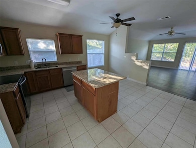 Kitchen with light tile patterned floors, appliances with stainless steel finishes, light stone counters, a center island, and brown cabinets