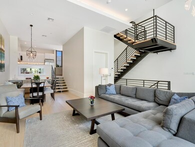 Living room with warm oak engineered hardwood flooring and architecturally featured 'floating' staircase with warm natural maple treads with view to dining room and kitchen.