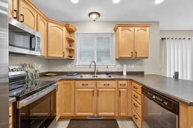 Kitchen with light brown cabinets, appliances with stainless steel finishes, a peninsula, dark countertops, and recessed lighting