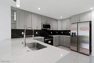 Kitchen featuring appliances with stainless steel finishes, light stone counters, backsplash, gray cabinets, and light marble finish floors