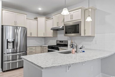 Kitchen featuring appliances with stainless steel finishes, a peninsula, backsplash, and decorative light fixtures