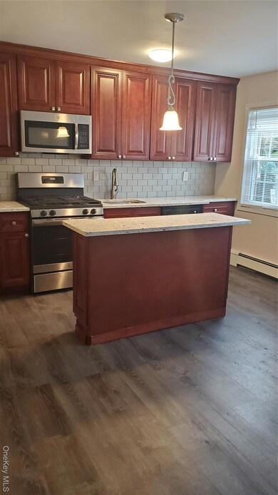 Kitchen with stove, tasteful backsplash, baseboard heating, dark wood-type flooring, and hanging light fixtures