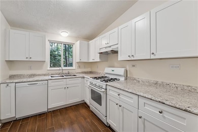 Kitchen featuring white appliances, white cabinetry, dark wood-style flooring, a textured ceiling, and under cabinet range hood