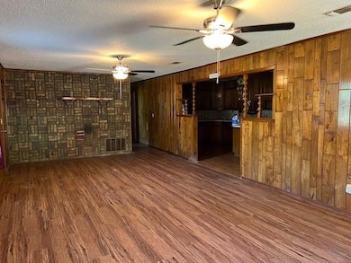 Unfurnished living room featuring dark wood-type flooring, a textured ceiling, ceiling fan, and wooden walls