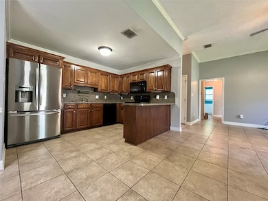 Kitchen with black appliances, a peninsula, tasteful backsplash, light tile patterned flooring, and ornamental molding