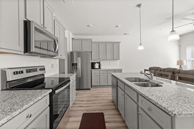 Kitchen with stainless steel appliances, gray cabinetry, light wood-style floors, and pendant lighting