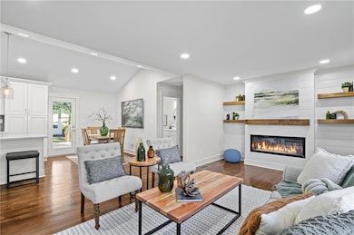 Living room with a glass covered fireplace, dark wood-style floors, recessed lighting, and vaulted ceiling