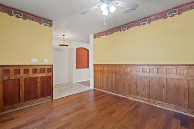 Spare room featuring wood finished floors, arched walkways, wooden walls, a ceiling fan, and a wainscoted wall